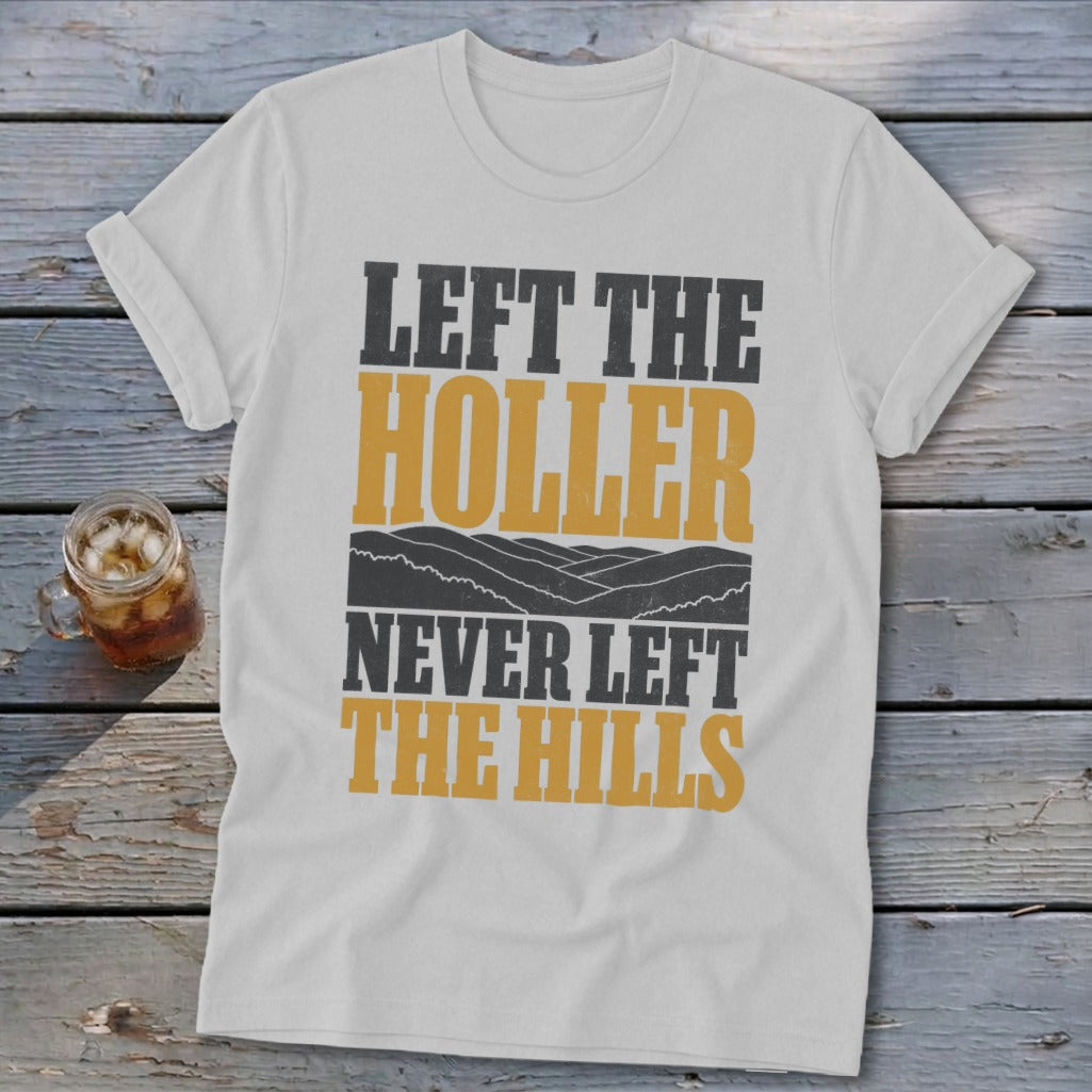 White t-shirt with text "LEFT THE HOLLER NEVER LEFT THE HILLS" and landscape graphic.