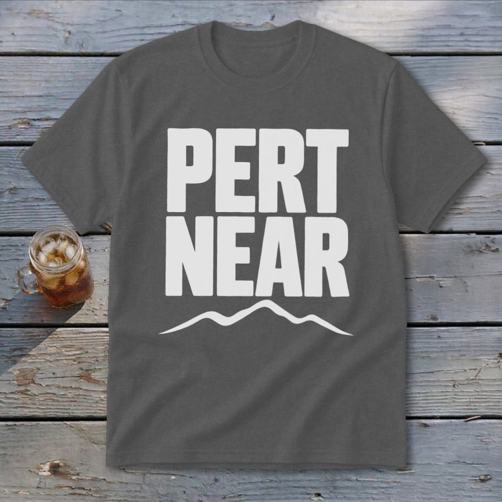 A gray t-shirt with white block text reading PERT NEAR above a mountain range graphic, laid on a wooden surface.