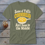 An olive green t-shirt with text and a skillet graphic, resting on a wooden surface.
