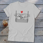 T-shirt with line drawing of couple and dog on swing, overlooking mountains.