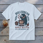 White t-shirt featuring a bear stirring apple butter, with text "HOLLERBEAR" and "APPLE BUTTER SEASON".