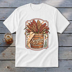White t-shirt graphic with a wooden barrel overflowing with sorghum stalks, text reads "Sorghum."