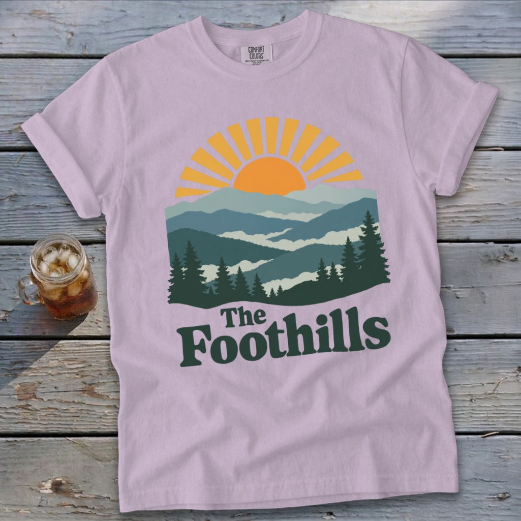Lilac t-shirt with a mountain sunrise graphic and "The Foothills" text.