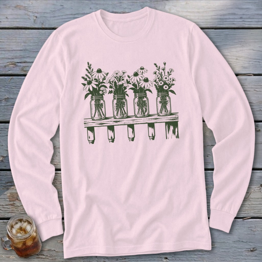 Light pink long-sleeve t-shirt featuring a green botanical illustration of four mason jars filled with wildflowers on a shelf.