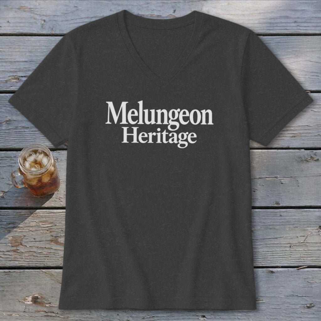 Dark gray V-neck T-shirt with white text reading Melungeon Heritage, lying on a rustic wooden surface.