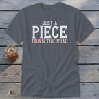 Gray t-shirt with white and pink text reading "JUST A PIECE DOWN THE ROAD."