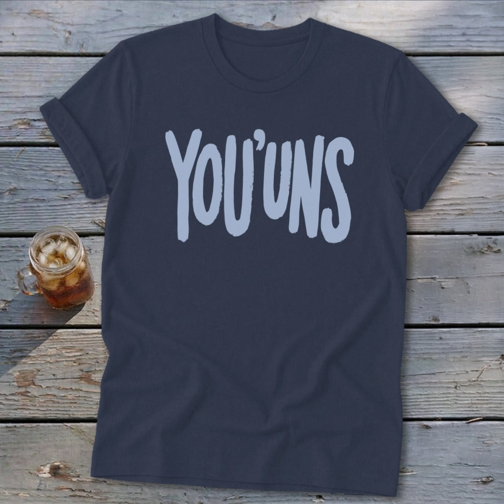 Navy t-shirt with light blue "YOU'UNS" text on a wooden background.