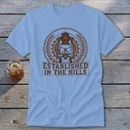 Light blue t-shirt with a brown lantern graphic and text "ESTABLISHED IN THE HILLS".