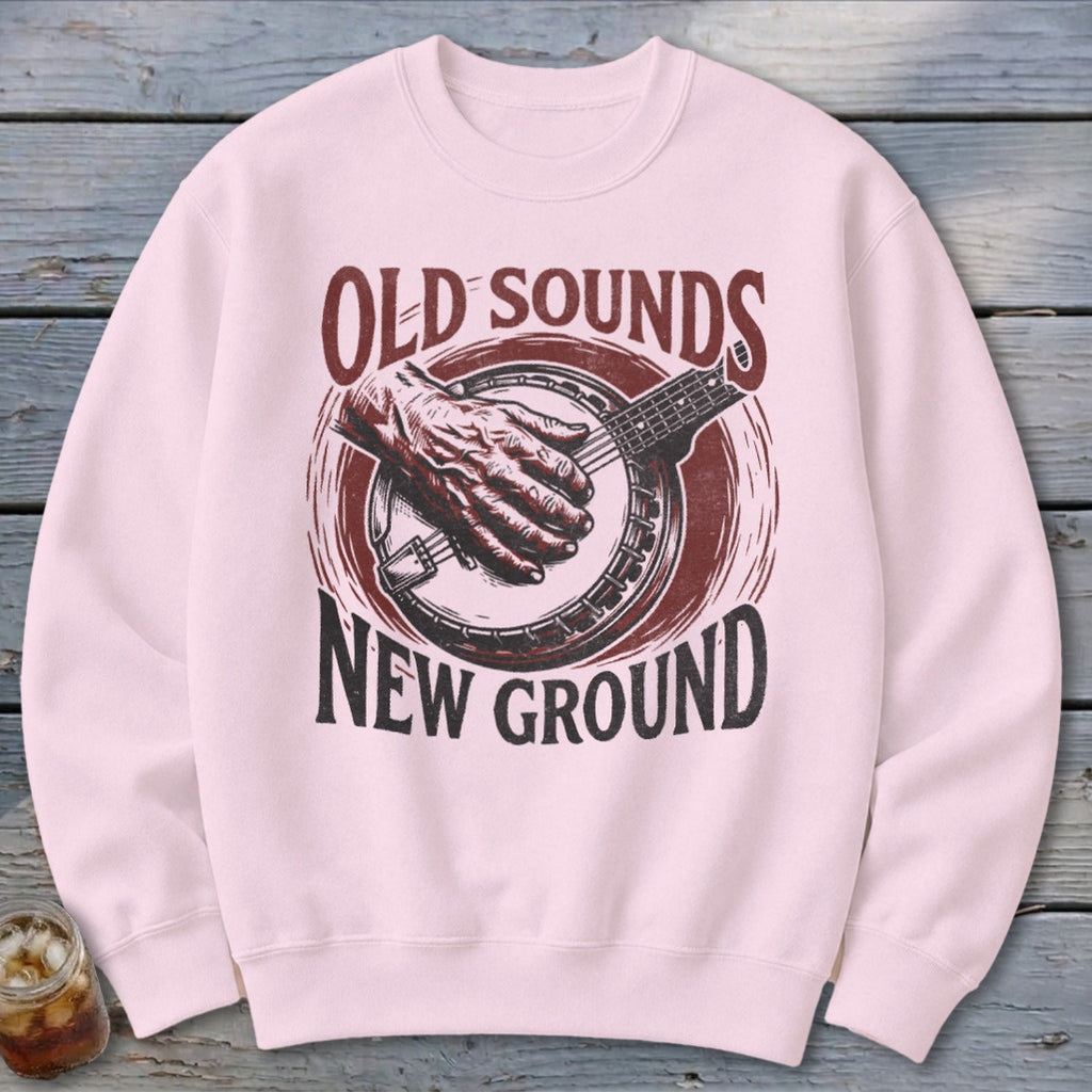 A light pink crewneck sweatshirt featuring a vintage banjo graphic with the text Old Sounds New Ground.