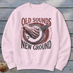 A light pink crewneck sweatshirt featuring a vintage banjo graphic with the text Old Sounds New Ground.