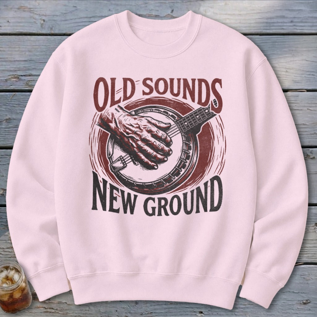 A light pink crewneck sweatshirt featuring a vintage banjo graphic with the text Old Sounds New Ground.