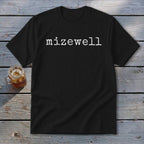 Black t-shirt with white text "mizewell" on a wooden surface next to a drink.