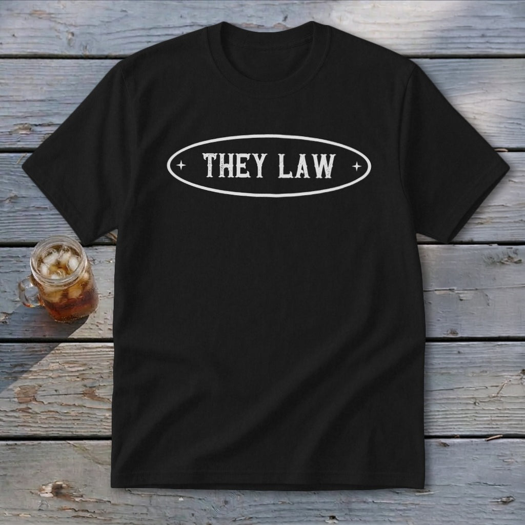 Black t-shirt with oval white text reading "THEY LAW" on weathered wood.