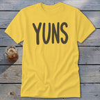 Yellow t-shirt with "YUNS" text and a glass of iced tea on a wooden background.