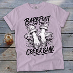 Light purple t-shirt with "Barefoot on the Creek Bank" graphic and bare feet in water.