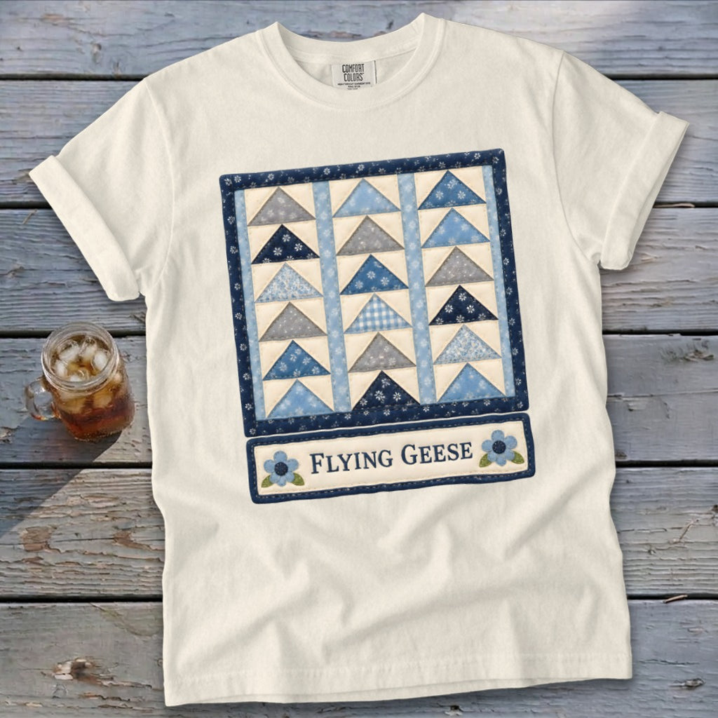 White t-shirt with a quilt block design featuring blue and grey triangles and text "Flying Geese".