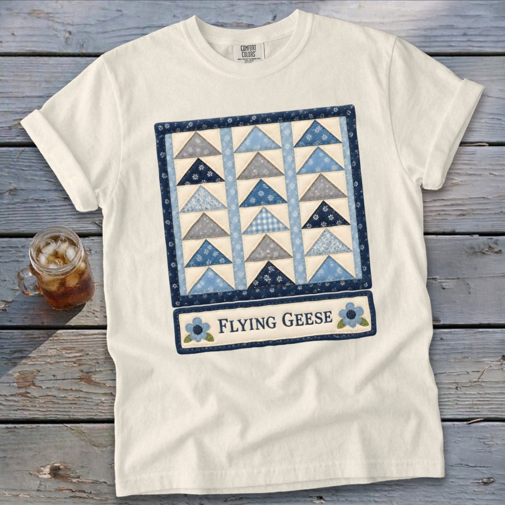 White t-shirt with a quilt block design featuring blue and grey triangles and text "Flying Geese".