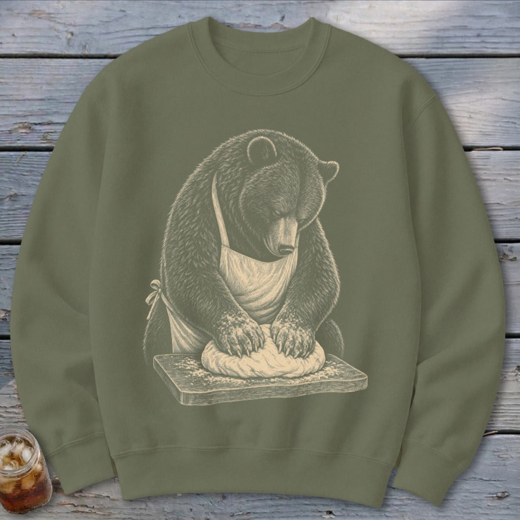 Bear wearing apron kneading dough on wooden board.