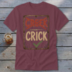 Maroon t-shirt with distressed sign reading "Creek" crossed out and "Crick" with checkmark.