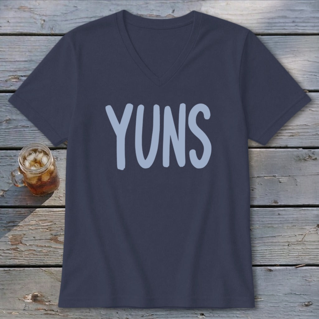 Navy v-neck t-shirt with light blue "YUNS" graphic, next to a drink.