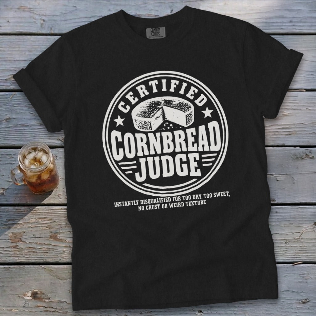 A black short-sleeve t-shirt features a white graphic with text reading Certified Cornbread Judge.