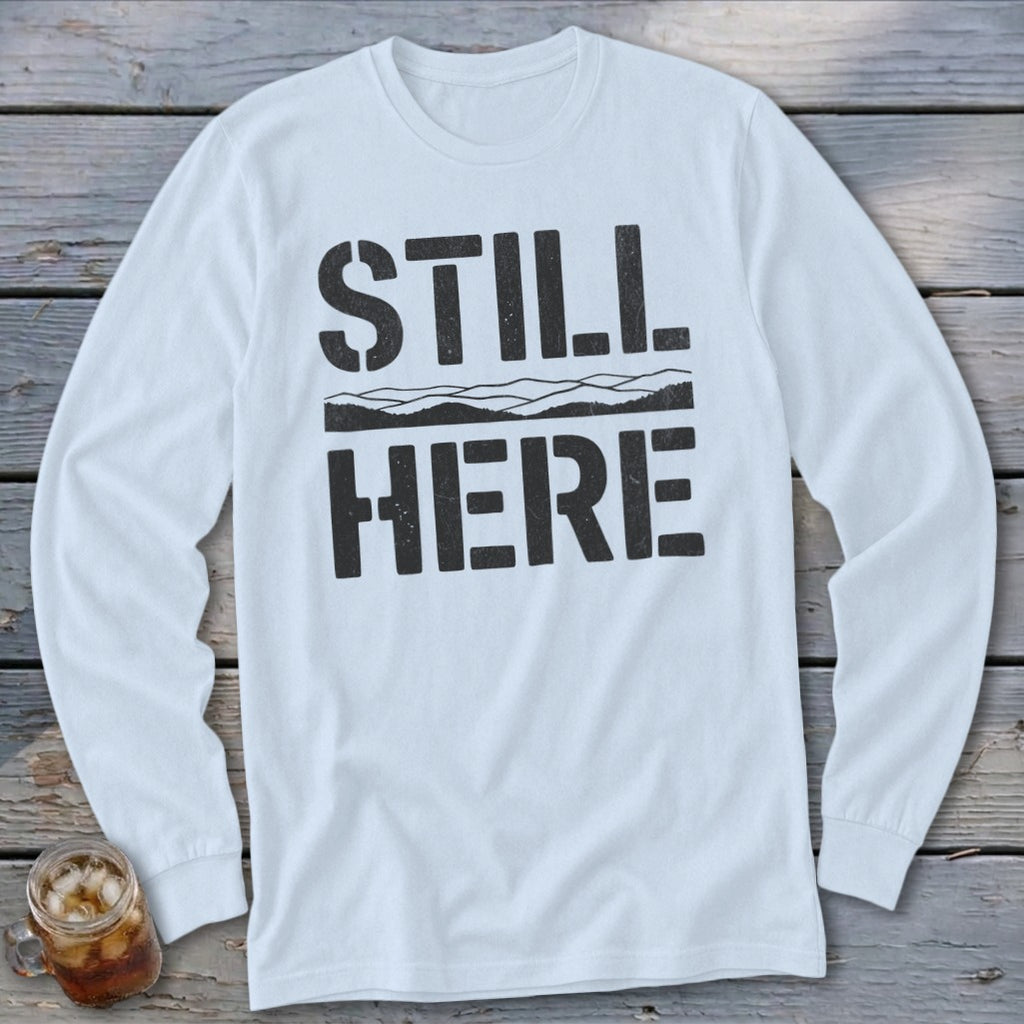 White long-sleeve shirt with black text "STILL HERE" and mountain graphic.