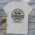 A light gray crewneck t-shirt featuring a circular graphic with text reading "Certified Cornbread Judge".