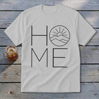 A light gray t-shirt featuring the word HOME in black line art, with a mountain and sun graphic replacing the letter O.