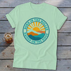 Light green t-shirt featuring a retro graphic of mountains and a sun with the text Born in the Holler Raised on the Ridge.