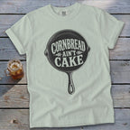 White Comfort Colors t-shirt with "Cornbread Ain't Cake" graphic on cast iron skillet.