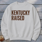 White crewneck sweatshirt with "KENTUCKY RAISED" text in brown.