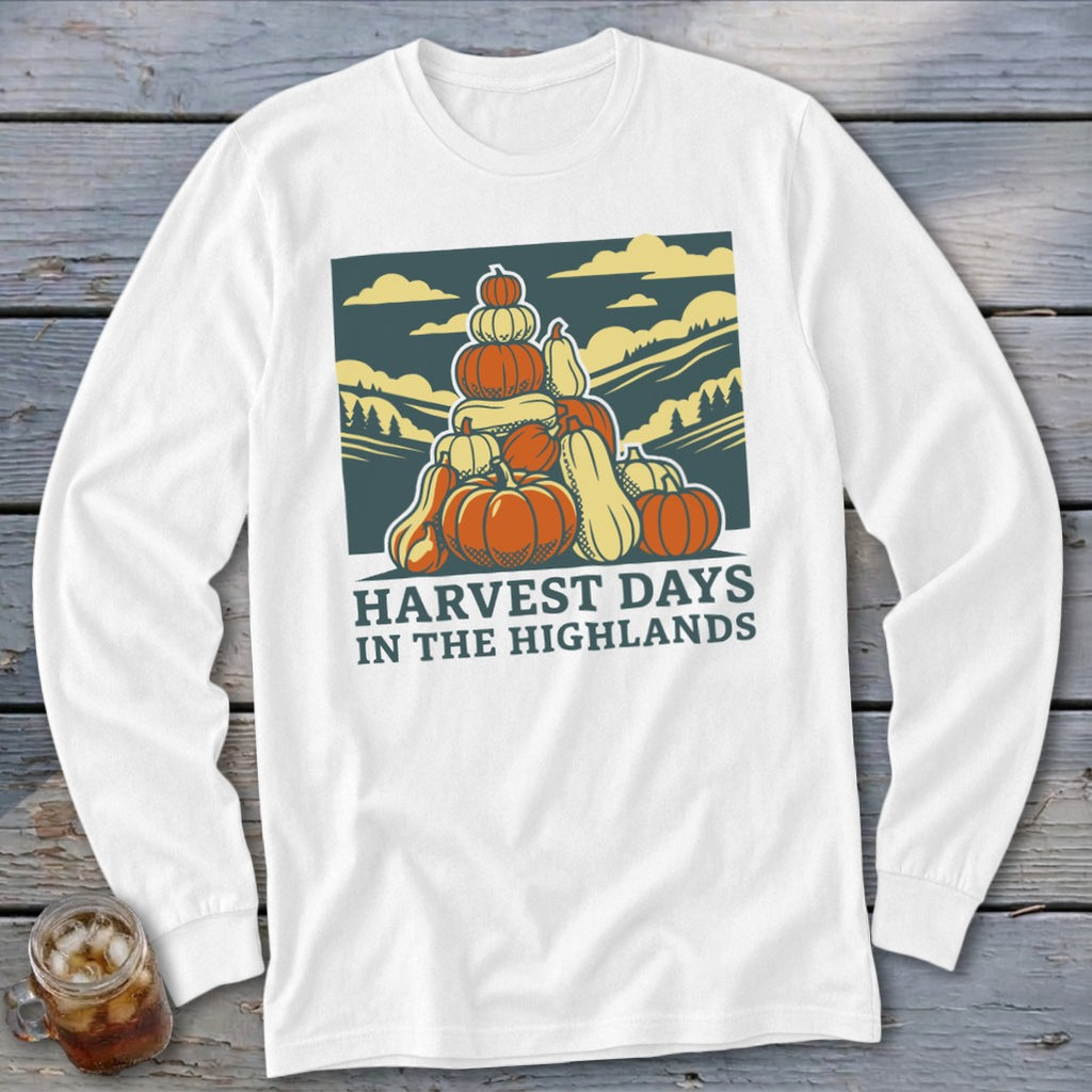 White long-sleeve t-shirt featuring a graphic of stacked pumpkins, hills, and the text Harvest Days in the Highlands.