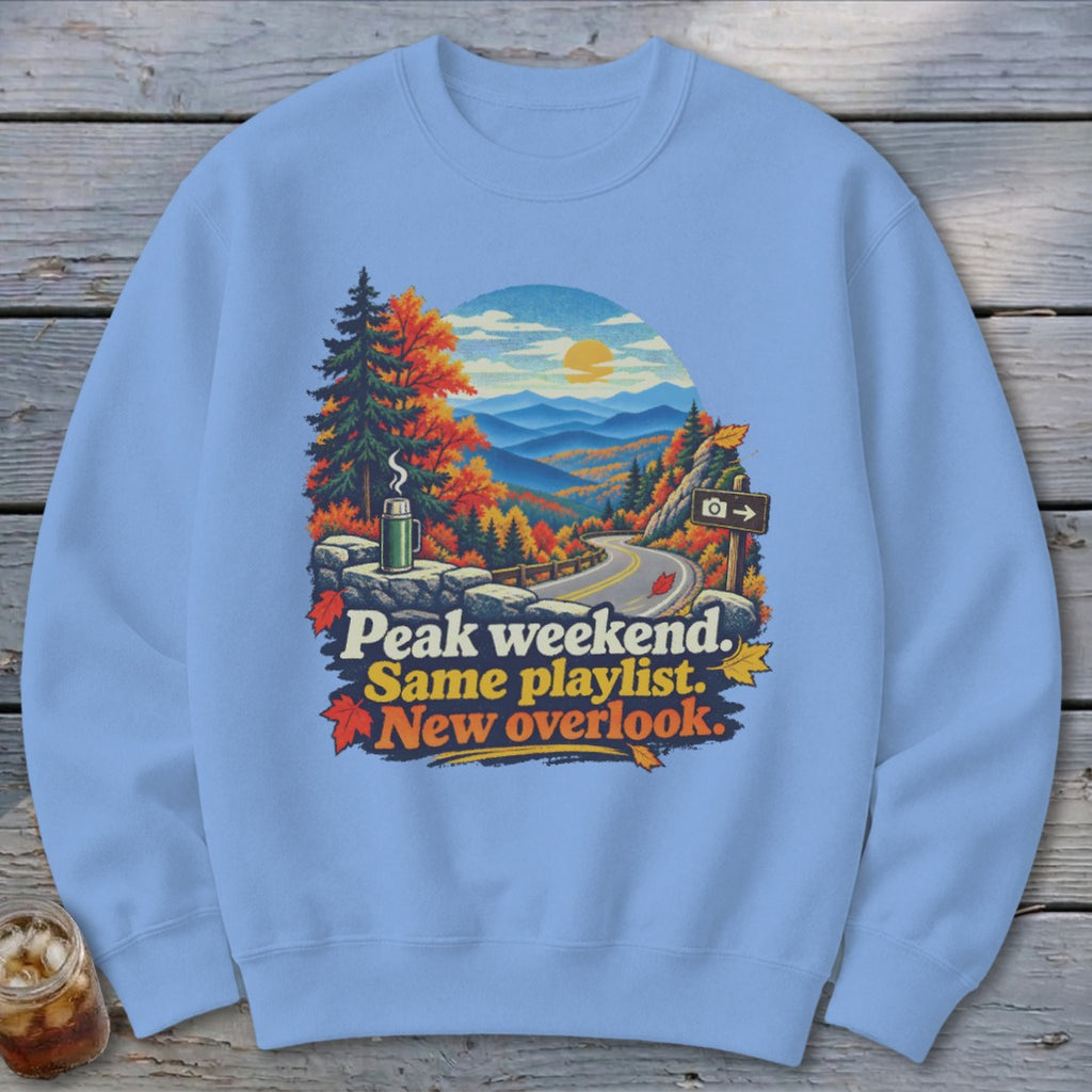 Sweatshirt with mountains, autumn trees, and text "Peak weekend. Same playlist. New overlook."