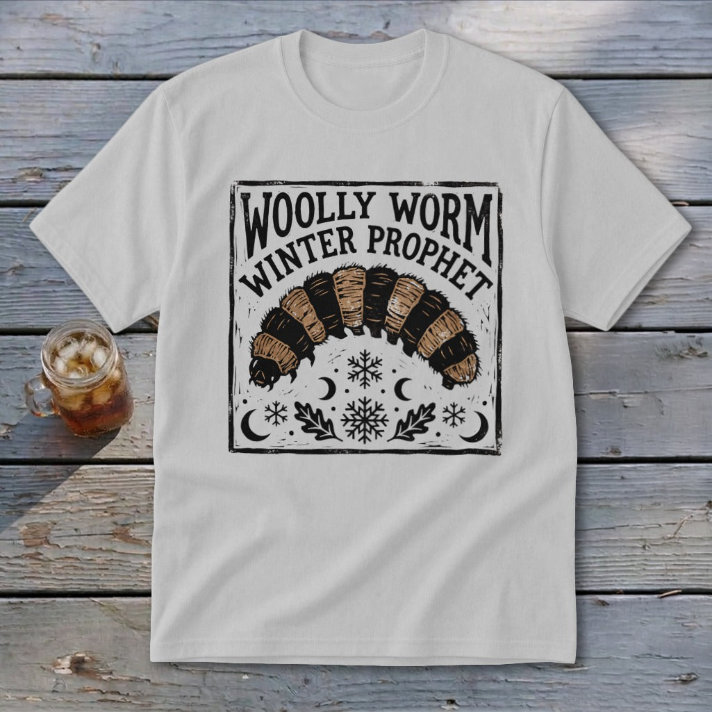 A light grey t-shirt featuring a black graphic of a woolly worm and text reading WOLLY WORM WINTER PROPHET.
