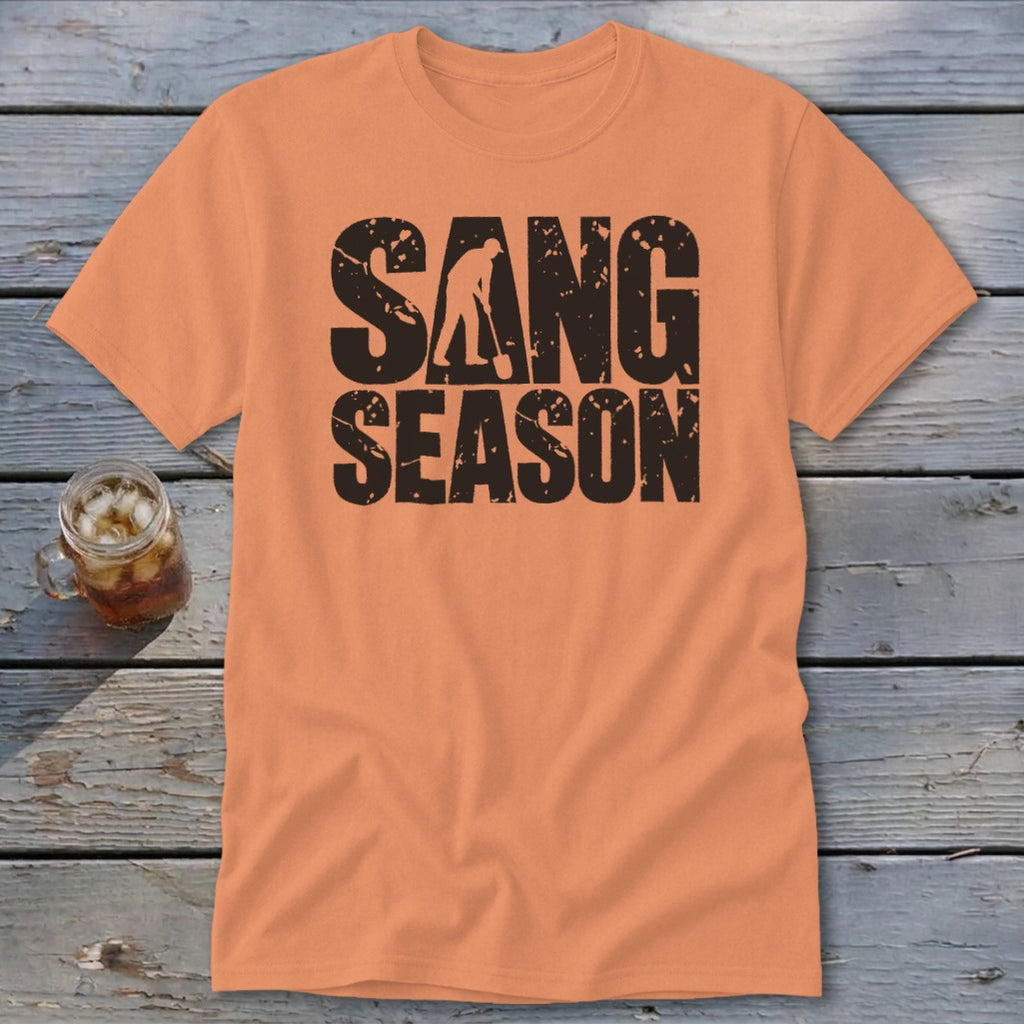 An orange t-shirt featuring distressed black text that reads SANG SEASON with a silhouette of a person digging.