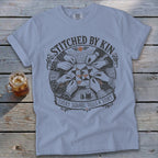 T-shirt with "STITCHED BY KIN EVERY SQUARE TELLS A STORY" text and hands quilting.