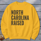 Yellow sweatshirt with "NORTH CAROLINA RAISED" text in dark gray.