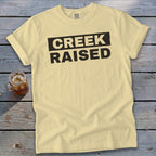 Yellow t-shirt with black text that reads "CREEK RAISED"