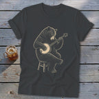 Bear sitting on stool playing a banjo on a dark gray t-shirt.