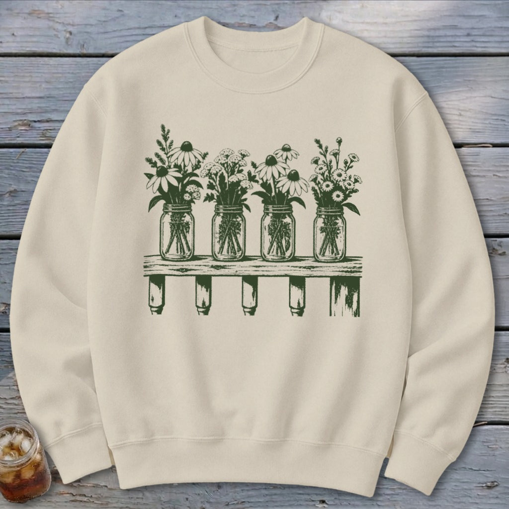 Beige crewneck sweatshirt with a green graphic of four mason jars filled with wildflowers on a wooden shelf.