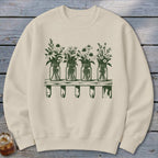 Beige crewneck sweatshirt with a green graphic of four mason jars filled with wildflowers on a wooden shelf.