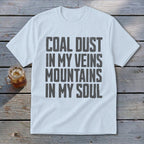 A white crewneck t-shirt featuring the dark grey distressed text COAL DUST IN MY VEINS MOUNTAINS IN MY SOUL centered on the chest.