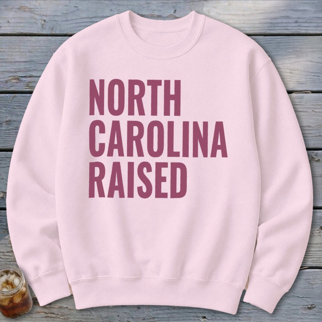 Light pink sweatshirt with "NORTH CAROLINA RAISED" text in maroon.