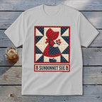 White t-shirt featuring a Sunbonnet Sue quilt block and text below.