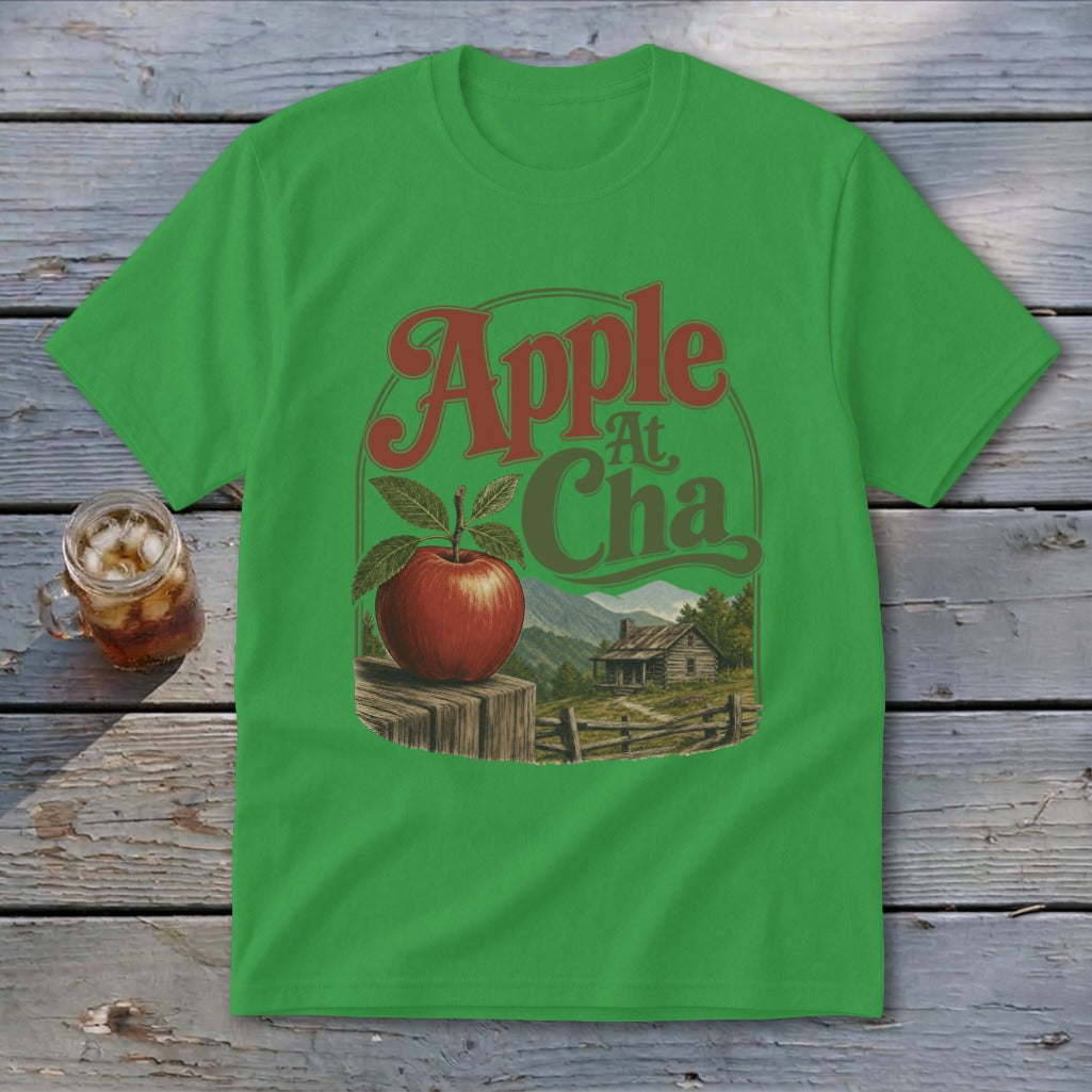 Grass-green short-sleeve t-shirt with a vintage-style graphic of an apple, mountains, and cabin, reading "Apple At Cha".