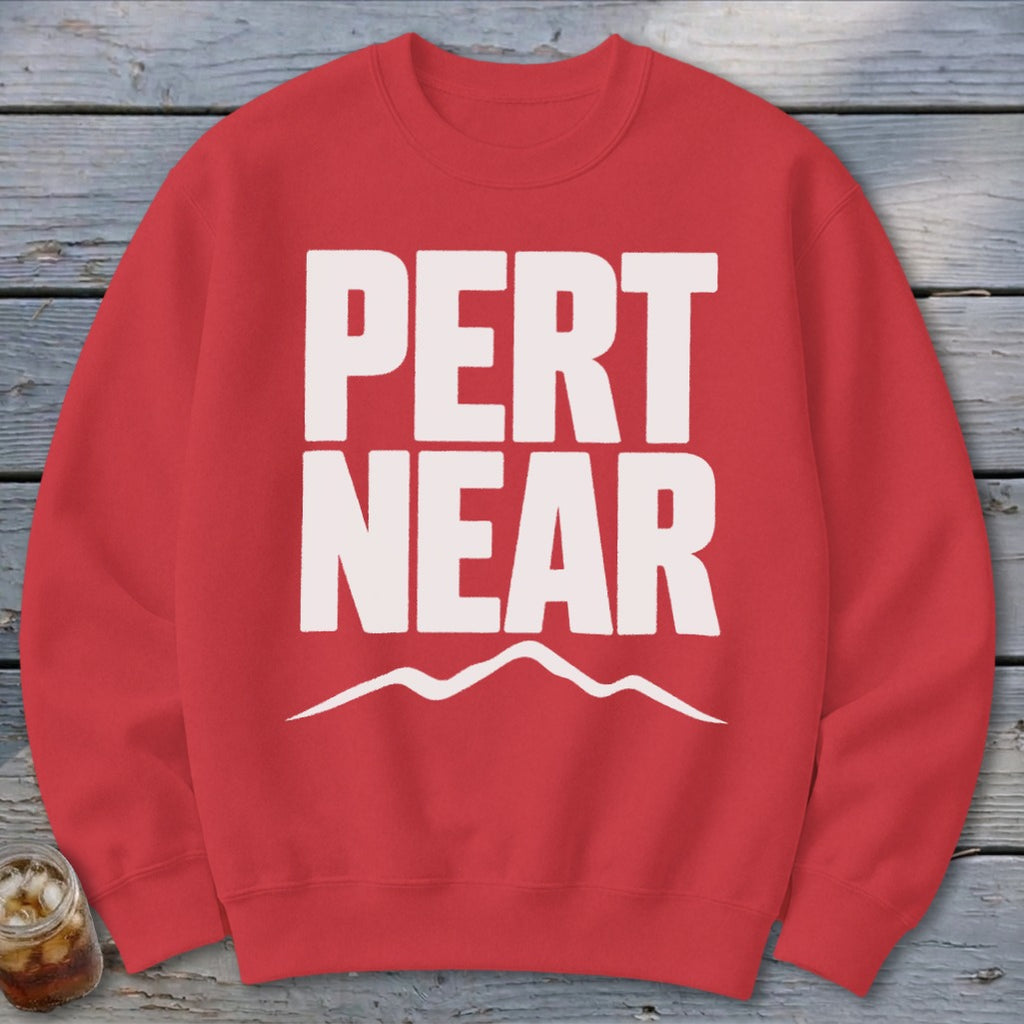 Red crewneck sweatshirt with large white text reading PERT NEAR above a minimalist mountain range graphic.