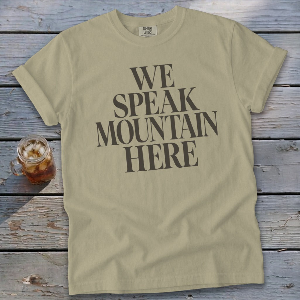 Tan t-shirt with dark gray text reading "WE SPEAK MOUNTAIN HERE".