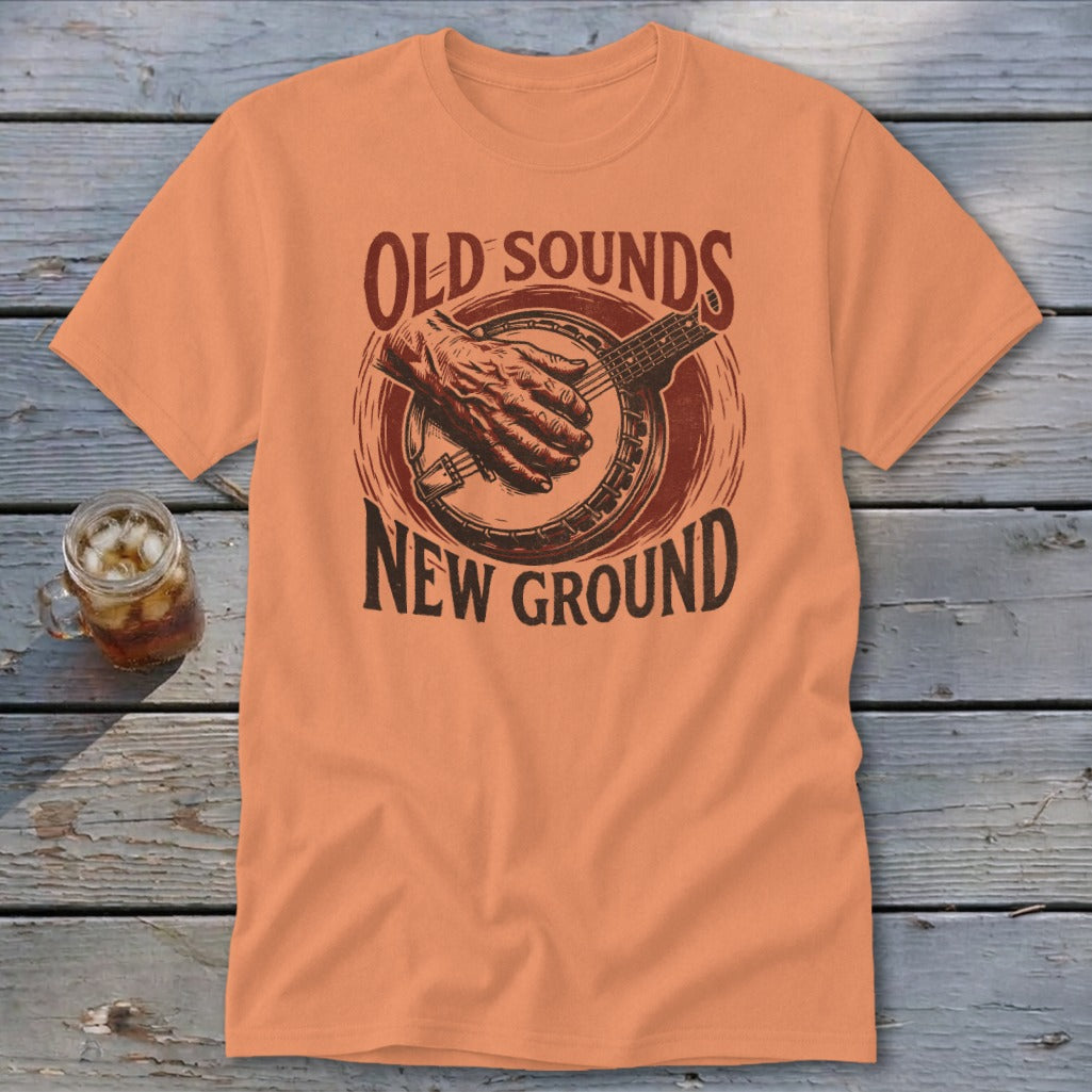 An orange t-shirt featuring a retro graphic of hands playing a banjo and text reading Old Sounds New Ground.