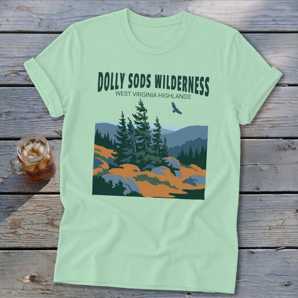 Light green t-shirt with a graphic of the Dolly Sods Wilderness and a drink on a wooden surface.