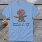 Light blue t-shirt with an anvil with a plant growing from it and text "FORGED IN FIRE ROOTED IN STONE".